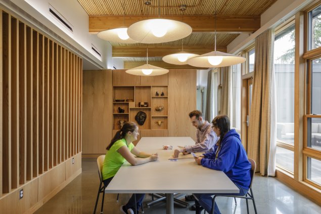 Three students sit at a dining table and play a card game. Light shines in through the windows connecting the dining and kitchen areas to an outdoor courtyard. The LIFTT curriculum that builds individual and collective agency amongst the program’s participants in order to inspire a life of independence and self-determination.